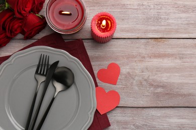 St. Valentine's day dinner. Romantic place setting with red roses, candles and decorative hearts on wooden table, flat lay. Space for text
