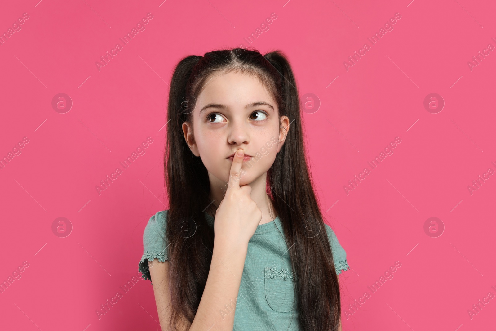 Photo of Portrait of pensive little girl on pink background. Thinking about answer for question