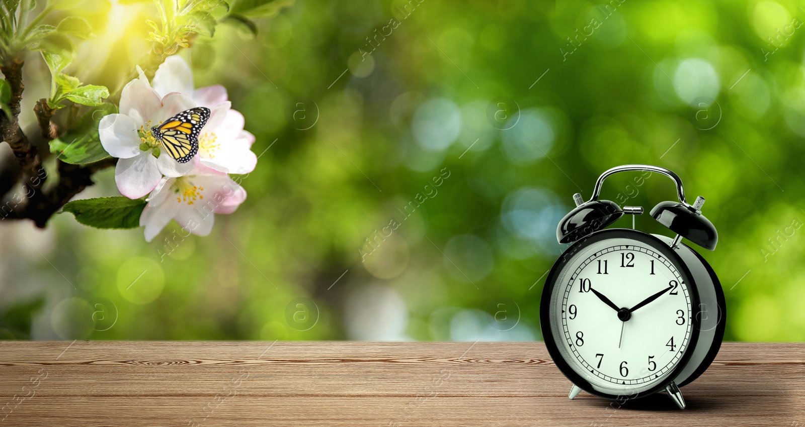Image of Black alarm clock on wooden table, space for text. Daylight saving time (Spring forward)