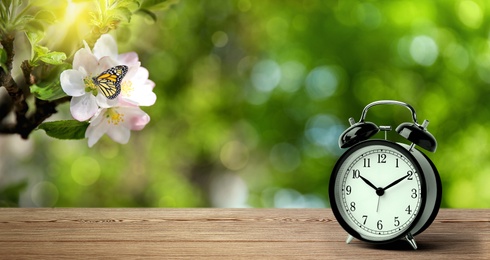 Black alarm clock on wooden table, space for text. Daylight saving time (Spring forward)