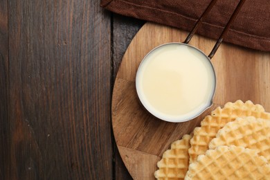 Photo of Tasty condensed milk and waffles on wooden table, top view. Space for text
