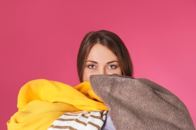 Photo of Young woman holding pile of dirty laundry on color background