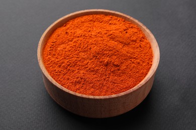 Photo of Aromatic paprika powder in wooden bowl on dark background