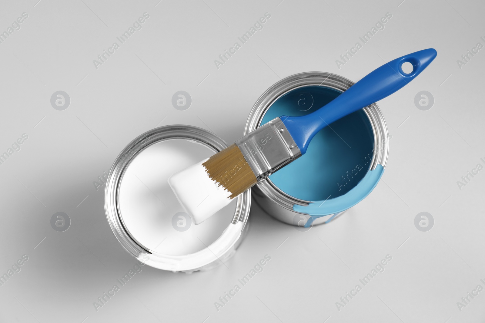 Photo of Cans of paints and brush on light blue background, flat lay