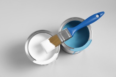Photo of Cans of paints and brush on light blue background, flat lay