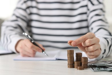 Financial savings. Woman stacking coins at white wooden table, closeup