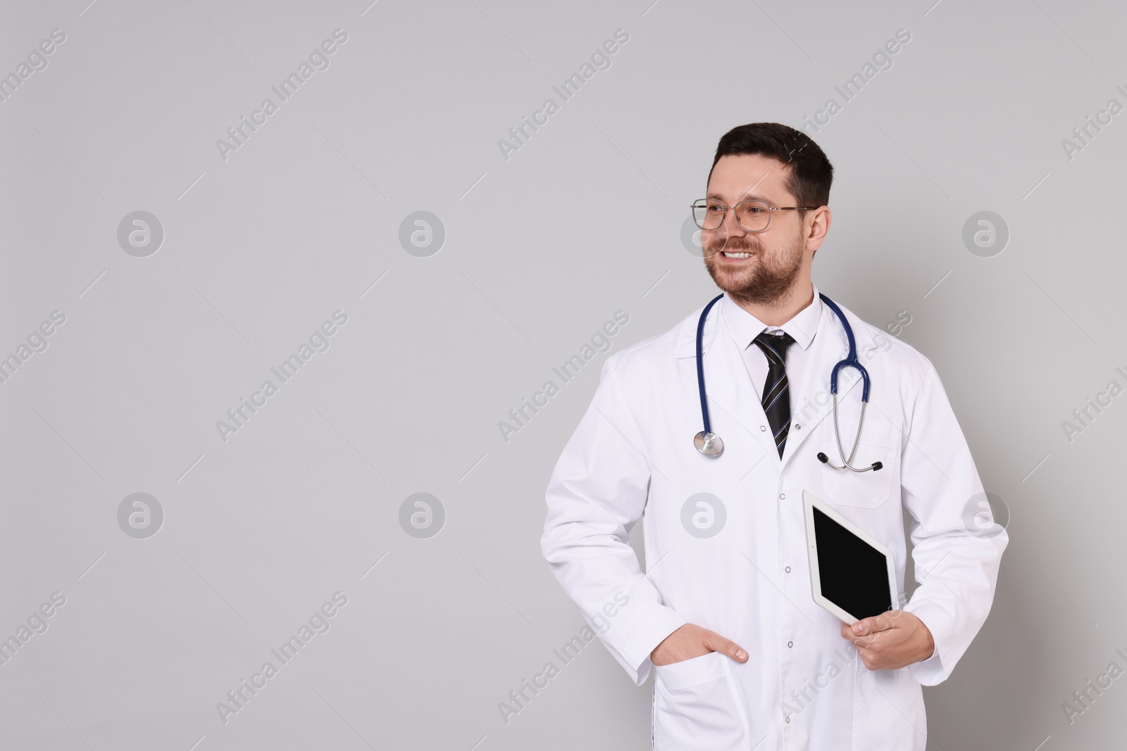 Photo of Portrait of smiling doctor with tablet on light grey background, space for text