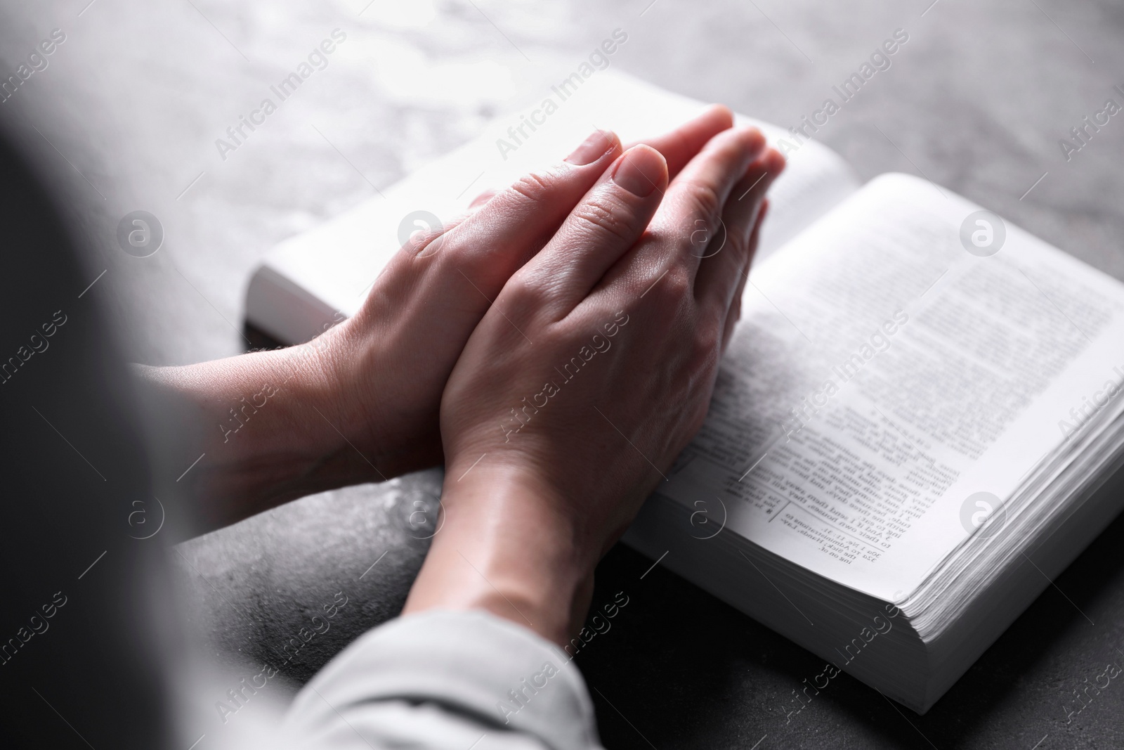 Photo of Religion. Christian woman praying over Bible at gray table, closeup