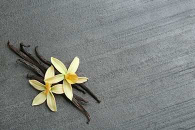 Flat lay composition with vanilla sticks and flowers on grey background. Space for text