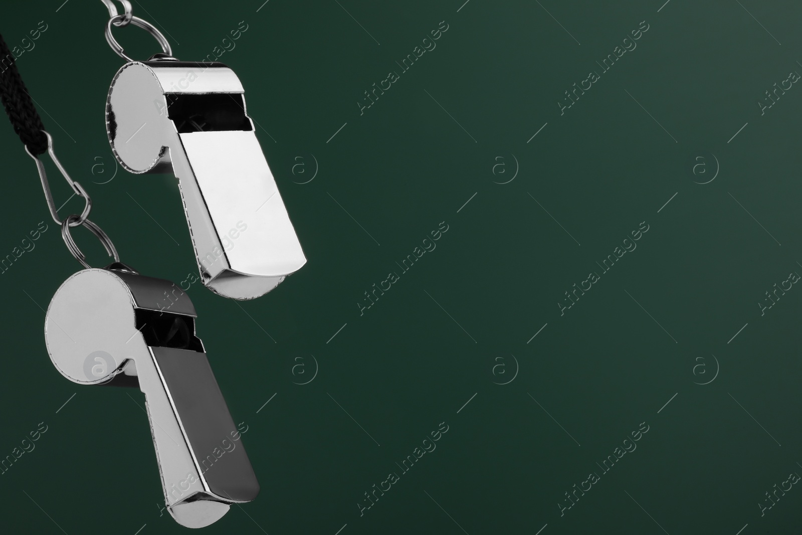 Photo of Referee equipment. Metal whistles on dark green background, closeup and space for text