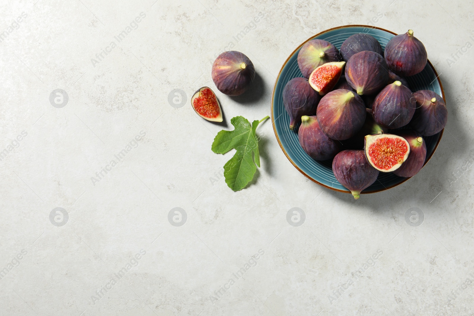 Photo of Plate with fresh ripe figs and green leaf on light table, flat lay. Space for text