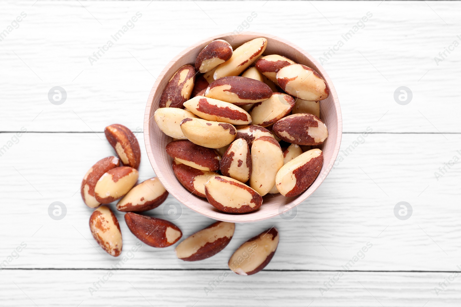 Photo of Bowl of delicious Brazil nuts on white wooden table, flat lay