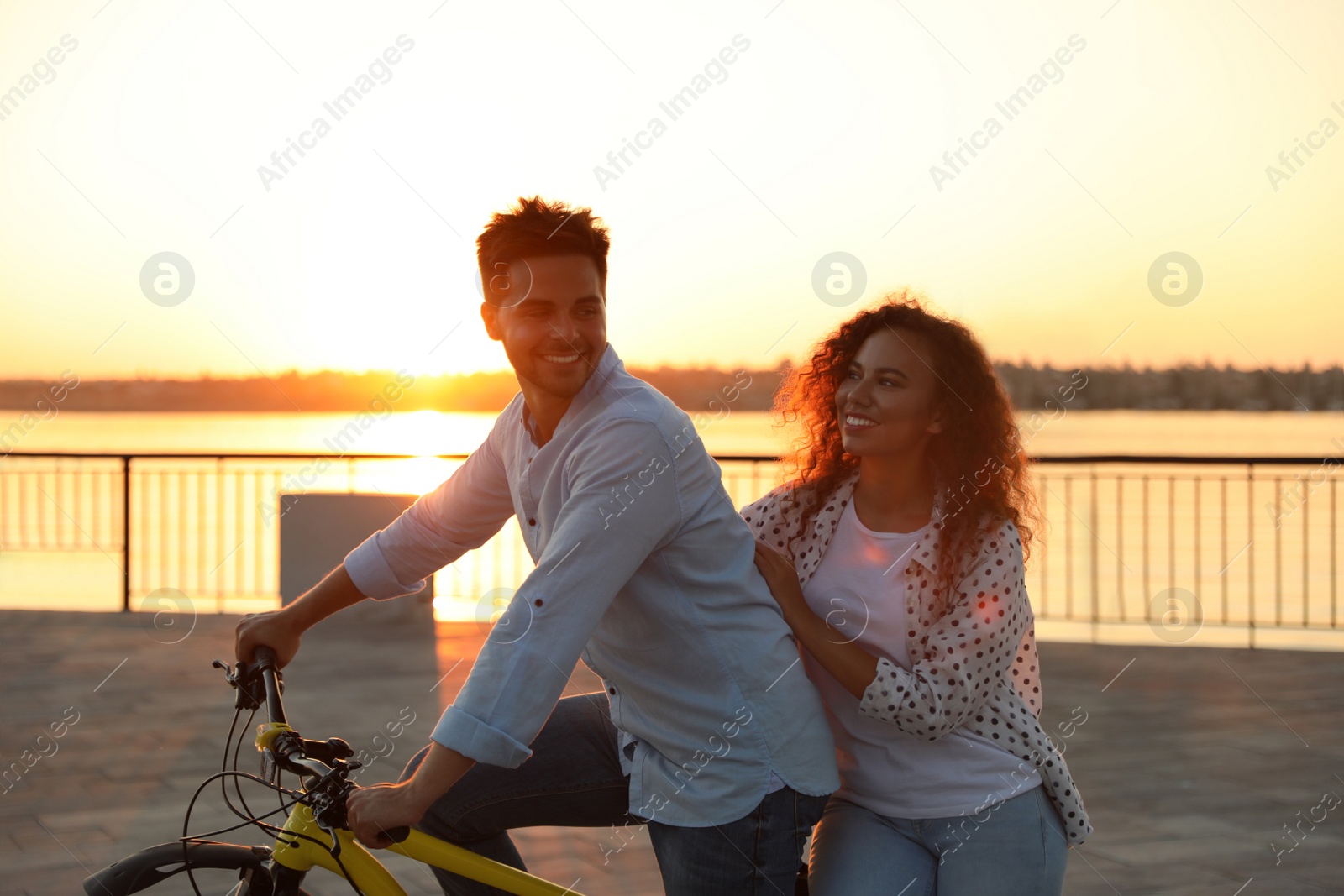 Photo of Young couple riding bicycle on city waterfront at sunset