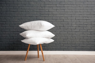 Photo of Pile of soft bed pillows on chair near brick wall with space for text