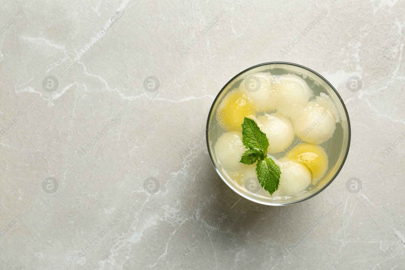 Photo of Glass of melon ball cocktail with mint on light grey marble table, top view. Space for text