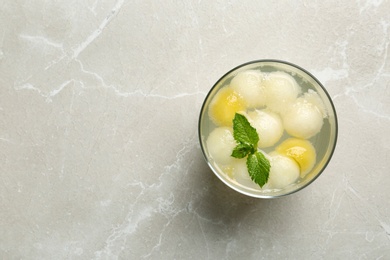 Photo of Glass of melon ball cocktail with mint on light grey marble table, top view. Space for text