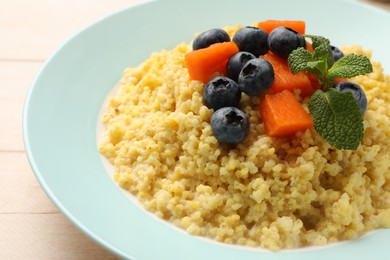 Plate with tasty millet porridge, blueberries, pumpkin and mint on light wooden table, closeup