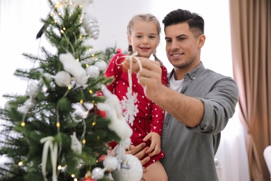 Photo of Happy father with his cute daughter decorating Christmas tree together at home