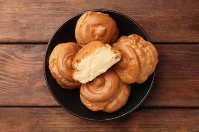Delicious profiteroles with cream filling on wooden table, top view