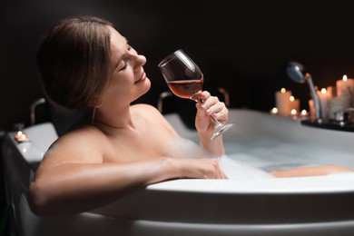 Beautiful woman drinking wine while taking bubble bath indoors. Romantic atmosphere