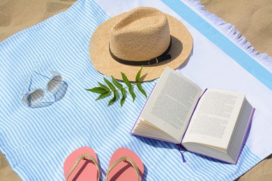 Photo of Beach towel with book, straw hat, sunglasses and flip flops on sand