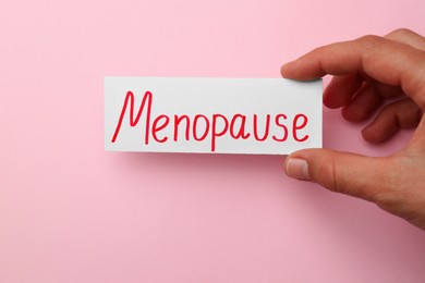 Photo of Woman holding card with word Menopause on pink background, closeup
