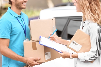 Photo of Young woman signing documents after receiving parcels from courier outdoors