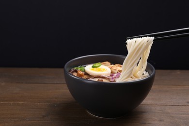 Photo of Eating delicious vegetarian ramen with chopsticks at wooden table against black background. Space for text