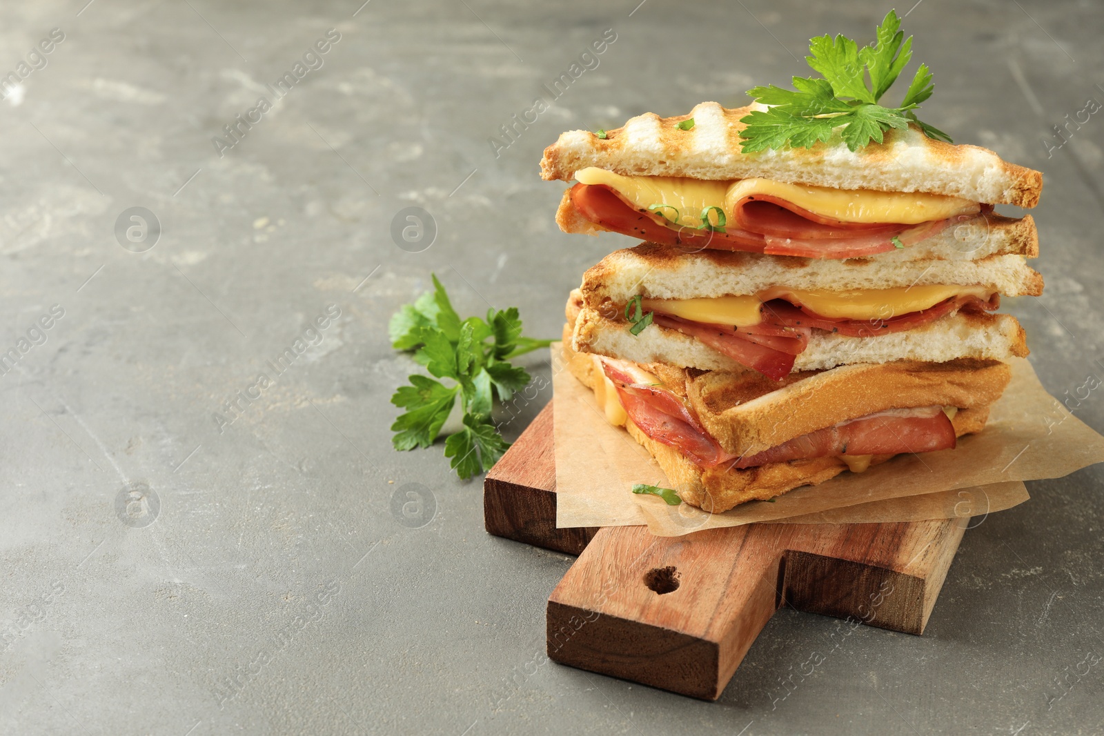 Photo of Stack of tasty sandwiches with ham, parsley and melted cheese on grey textured table, closeup. Space for text