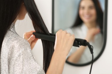 Woman using hair iron near mirror indoors, closeup. Space for text