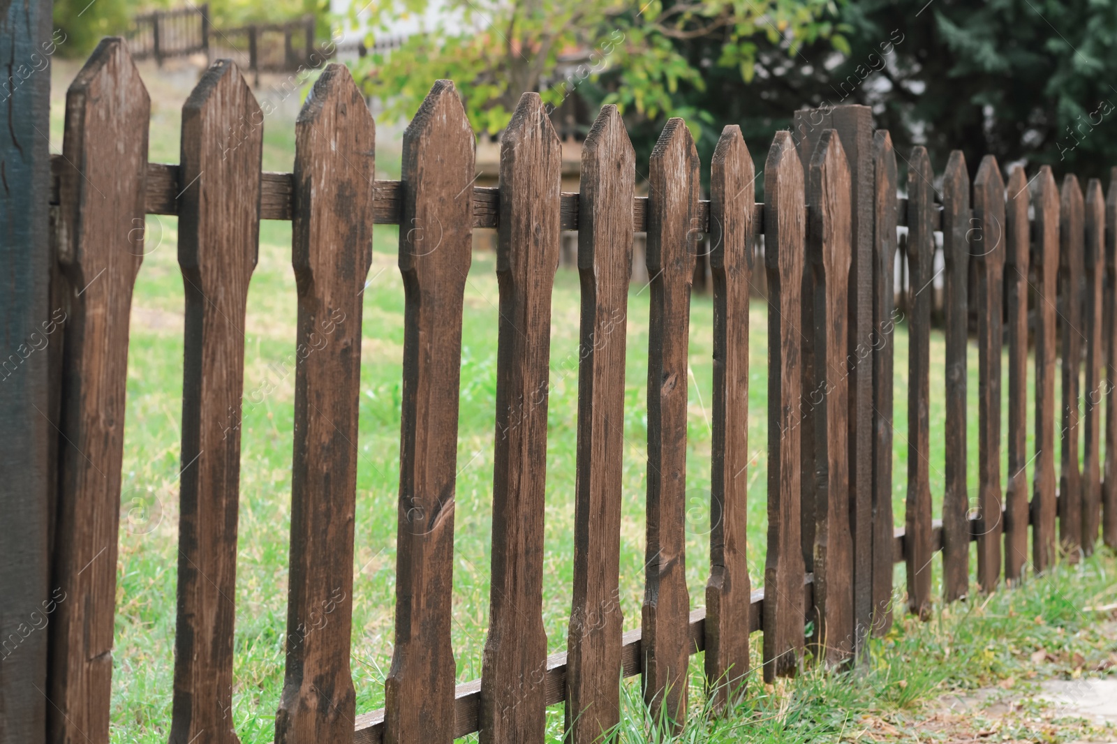 Photo of Low wooden fence near trees and green grass outdoors