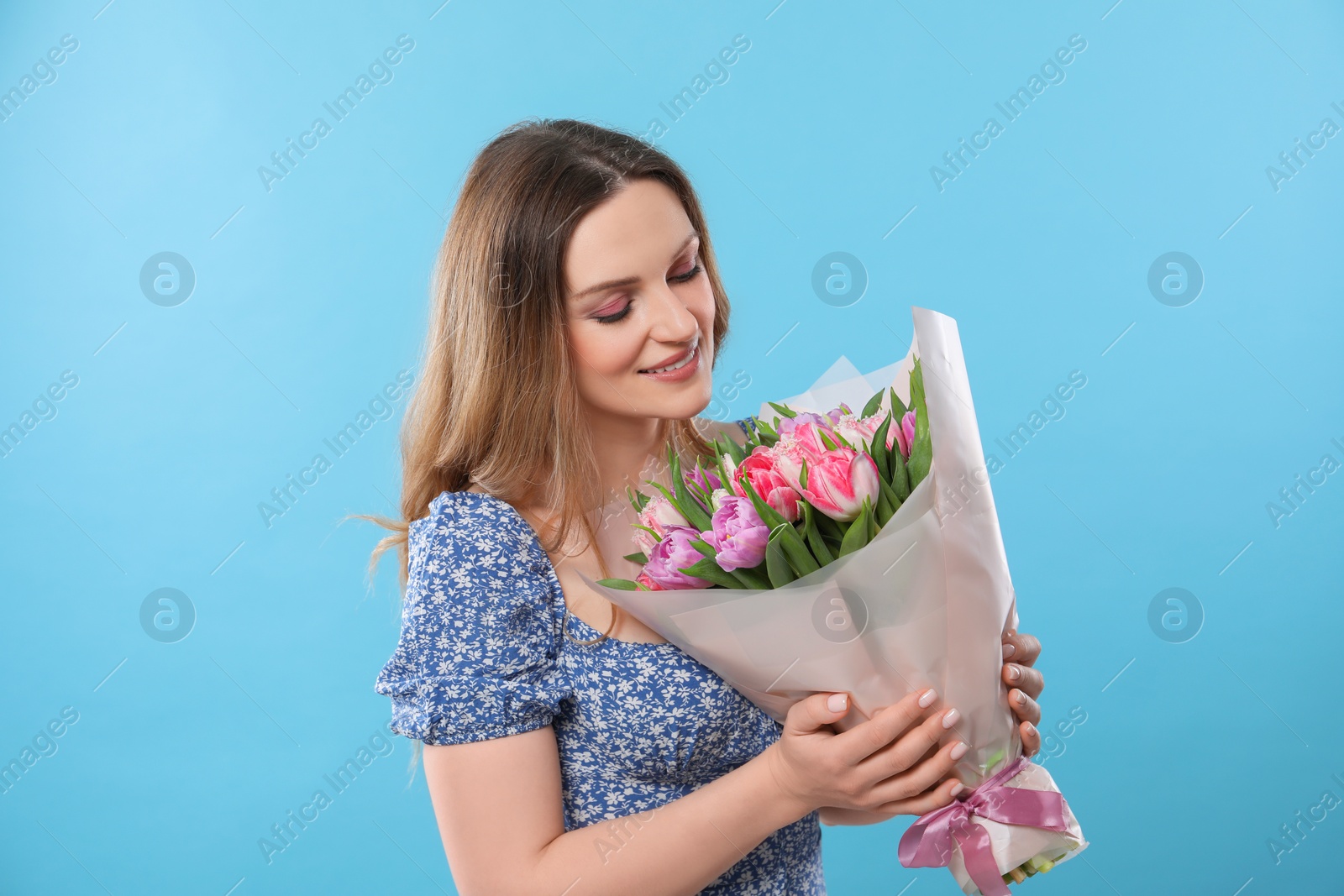 Photo of Happy young woman with bouquet of beautiful tulips on light blue background