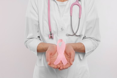 Doctor with stethoscope holding pink ribbon on white background, closeup. Breast cancer awareness