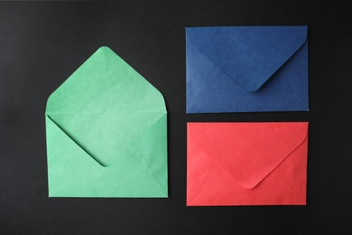Photo of Colorful paper envelopes on black background, flat lay