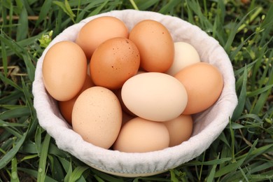 Photo of Fresh chicken eggs in basket on green grass outdoors, closeup
