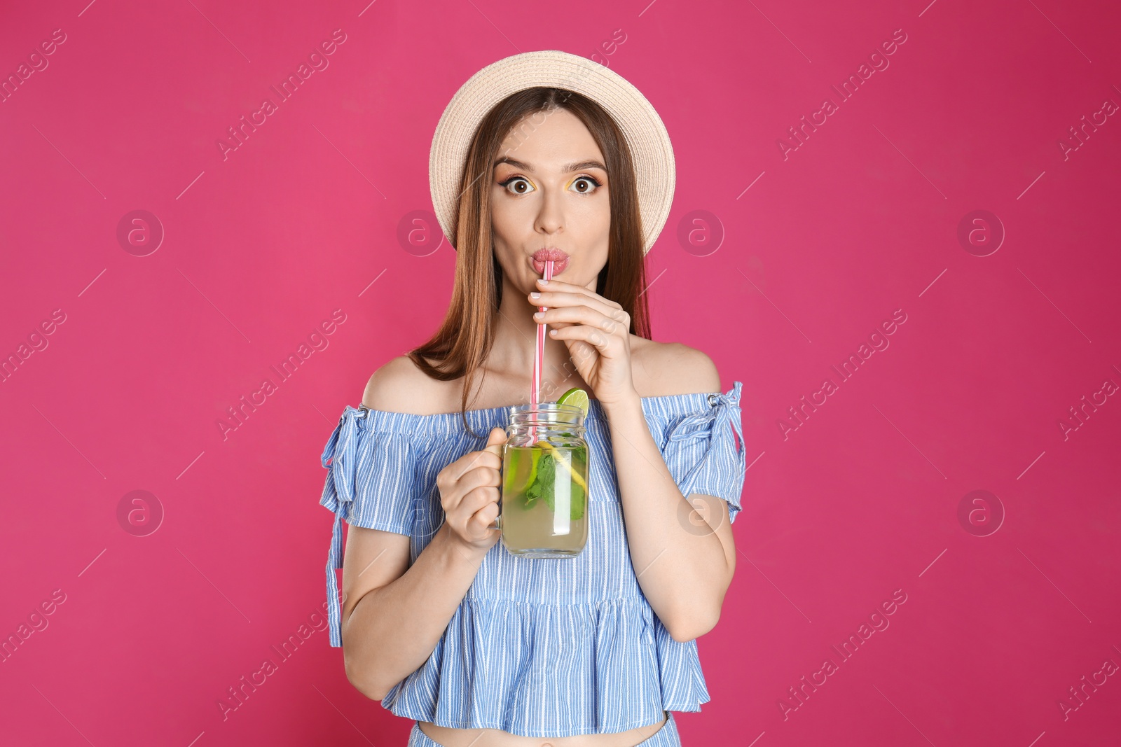 Photo of Emotional young woman drinking natural detox lemonade on pink background