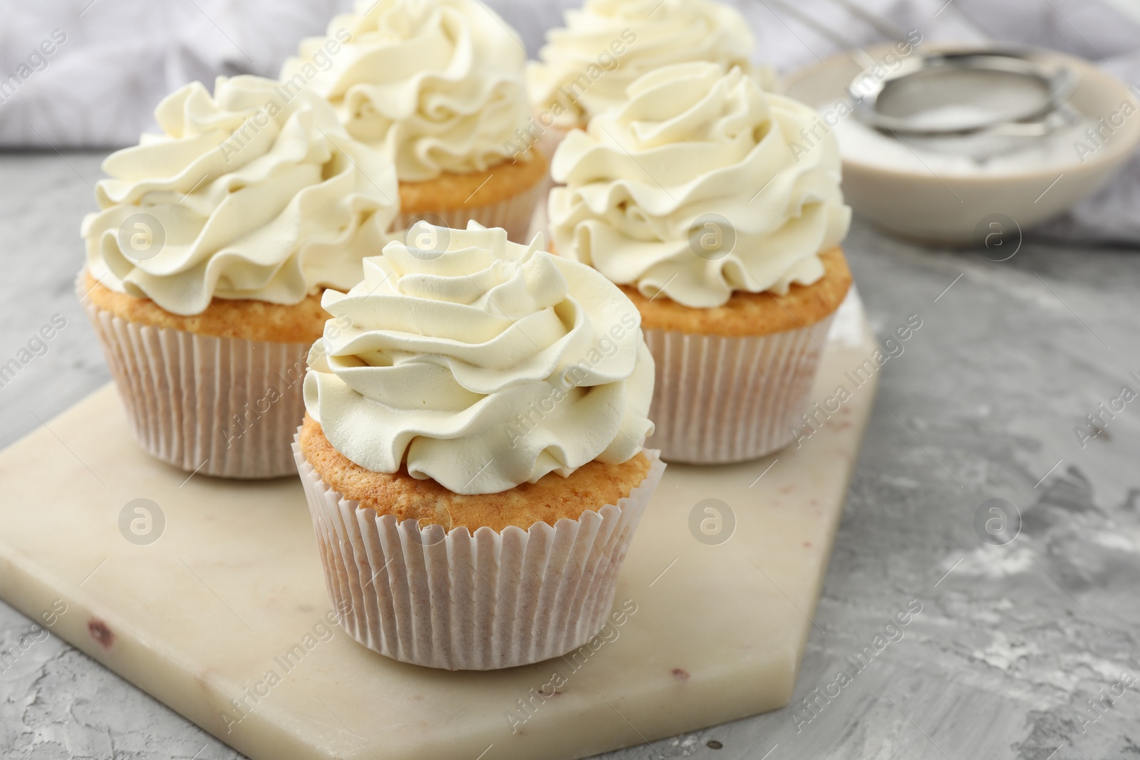 Photo of Tasty cupcakes with vanilla cream on grey table, closeup