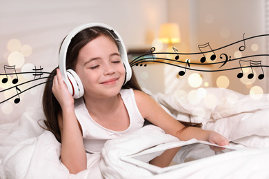 Cute little girl with tablet listening to music through headphones in bed at home