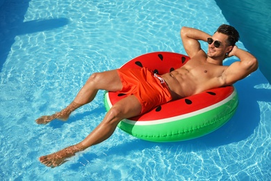 Young man with inflatable ring in pool on sunny day