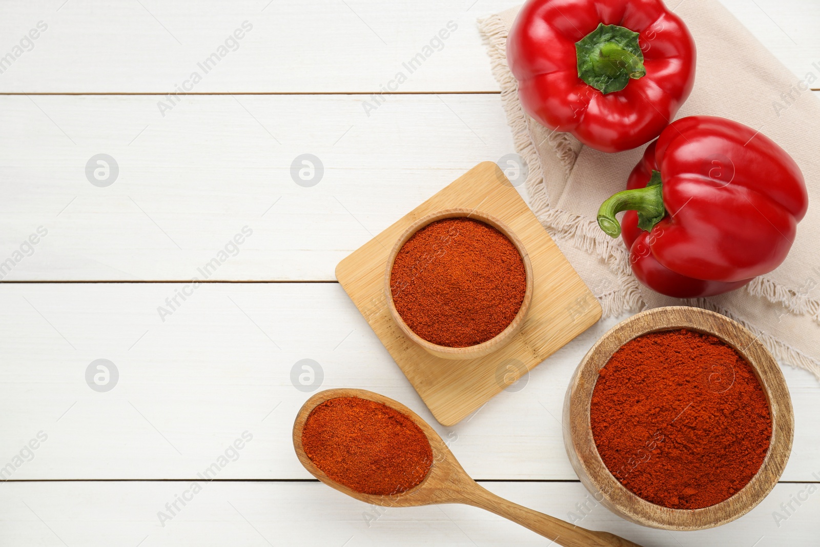 Photo of Bowls, spoon with aromatic paprika powder and fresh bell peppers on white wooden table, flat lay. Space for text