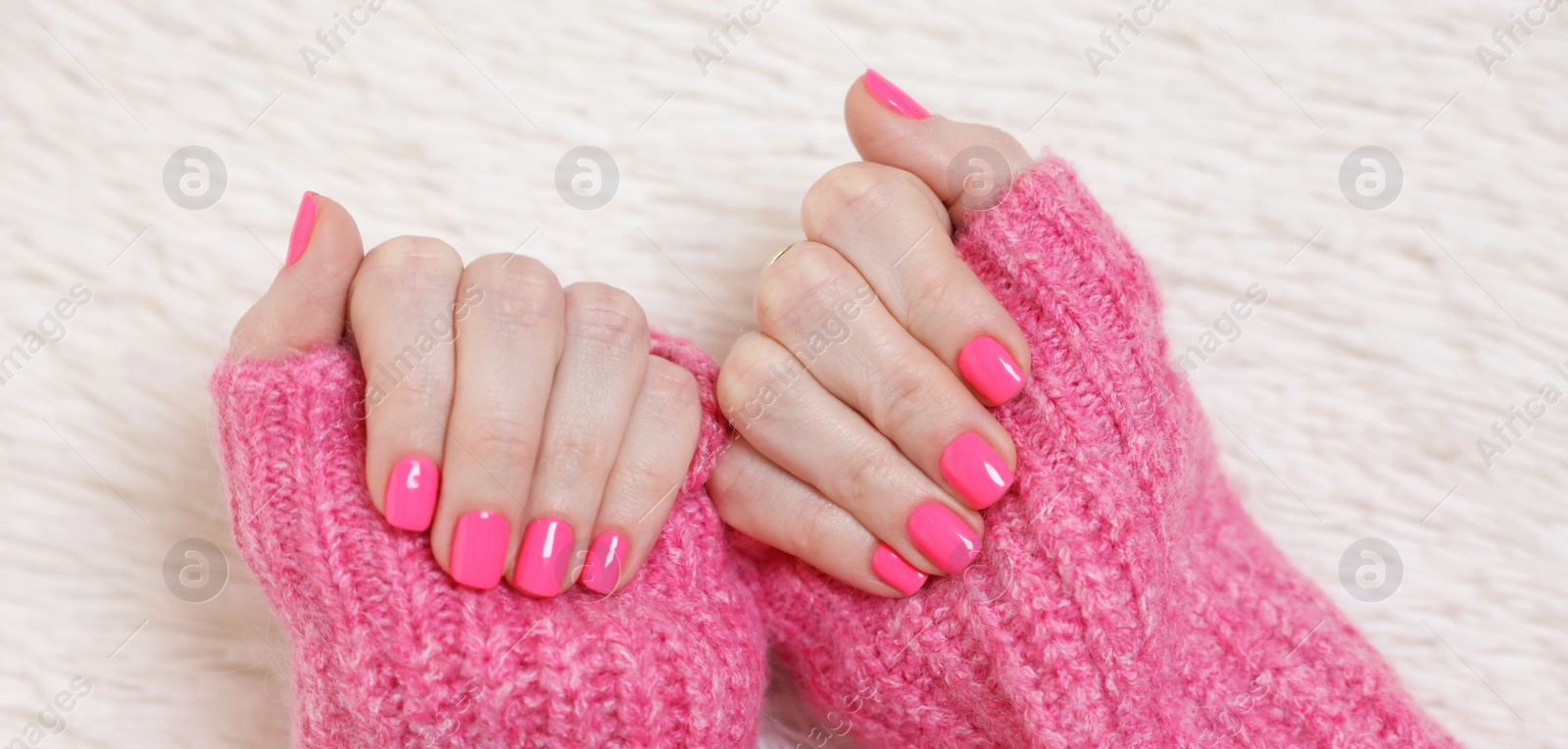 Photo of Woman showing her manicured hands with pink nail polish on faux fur mat, top view