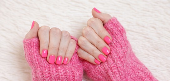 Woman showing her manicured hands with pink nail polish on faux fur mat, top view