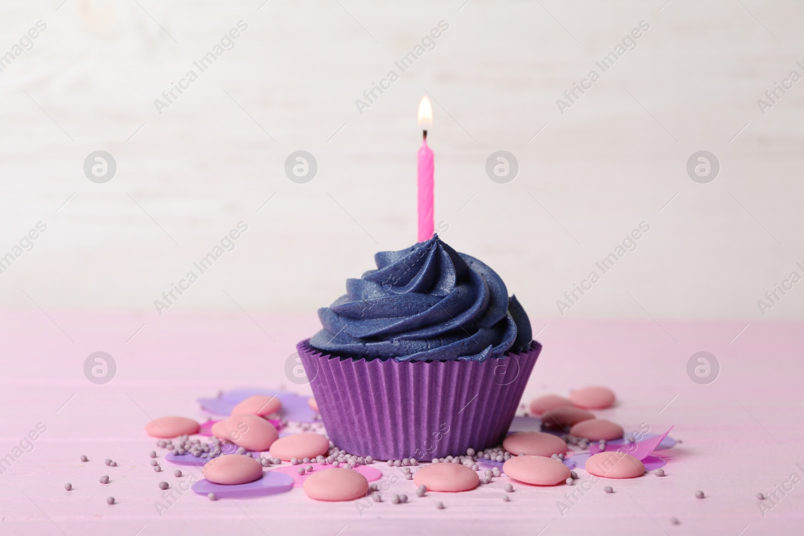 Photo of Delicious birthday cupcake with cream and burning candle on pink table