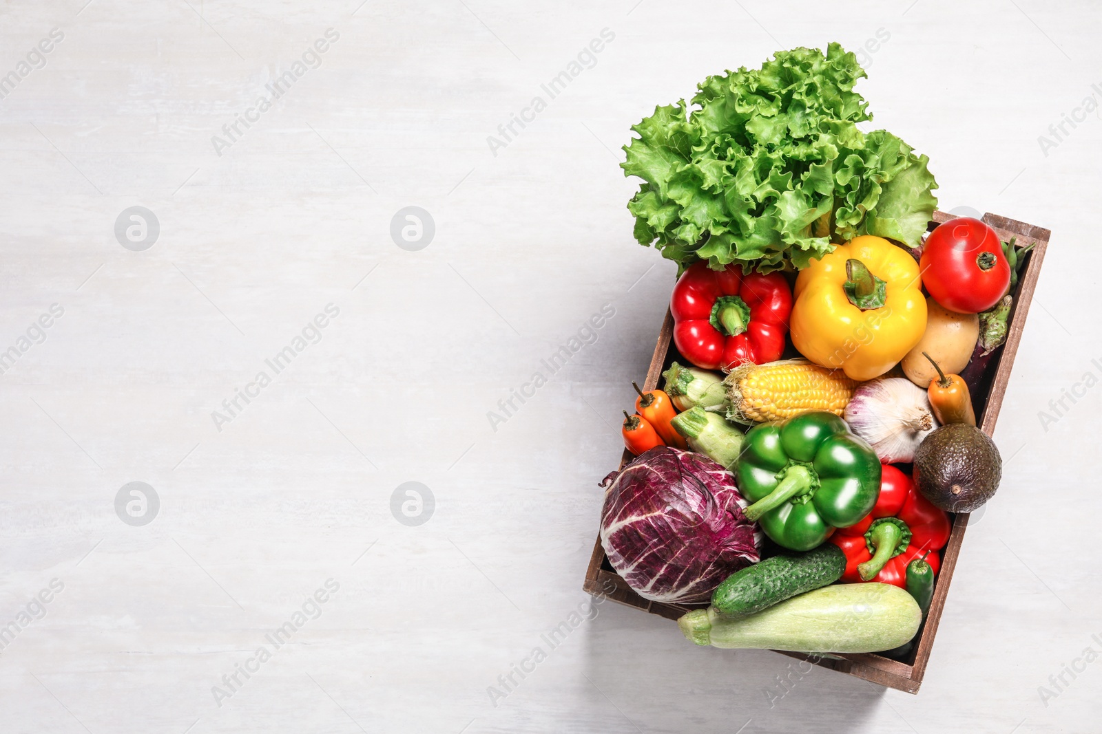 Photo of Crate with different fresh vegetables on light background, top view. Space for text