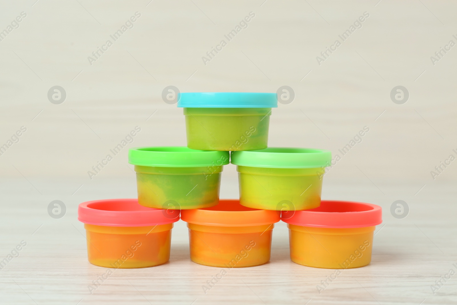 Photo of Plastic containers with colorful play dough on white wooden table