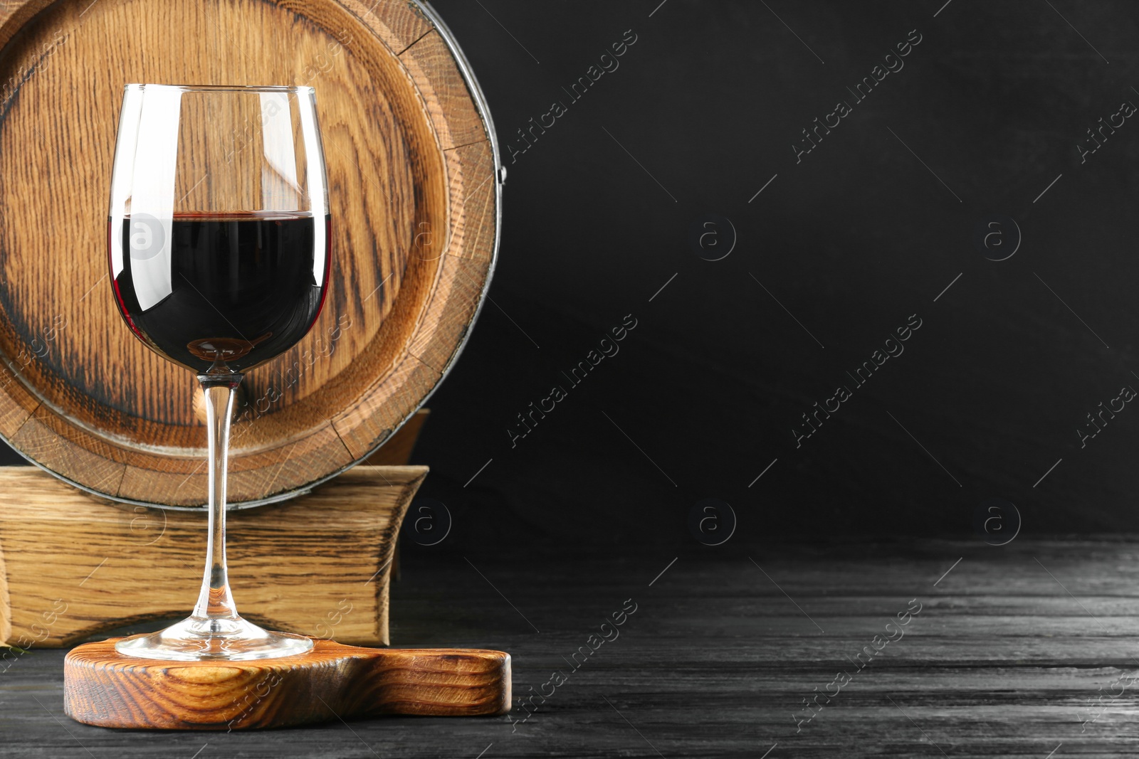 Photo of Wooden barrel and glass with delicious wine on black table, space for text