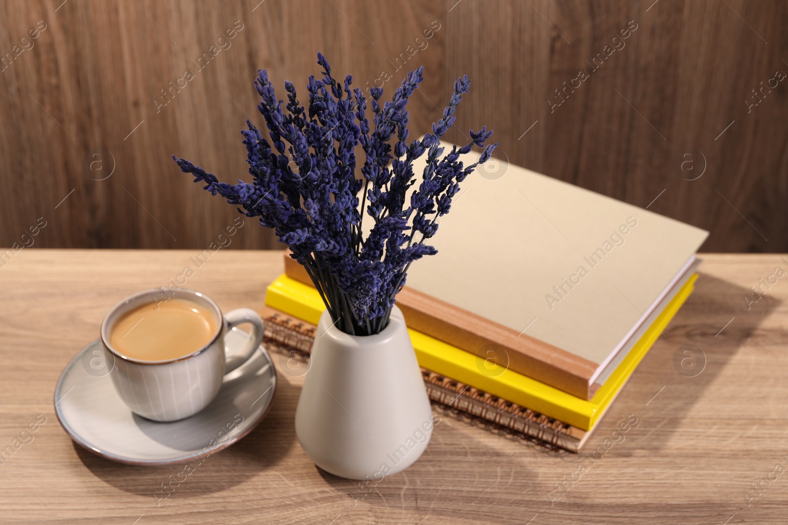 Photo of Bouquet of beautiful preserved lavender flowers, notebooks and cup of coffee on wooden table indoors