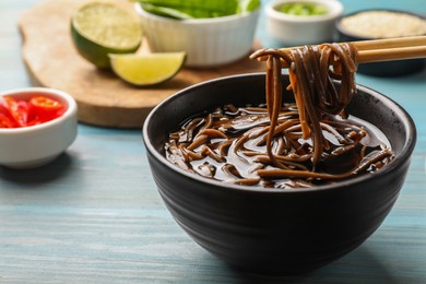 Photo of Eating delicious buckwheat noodle (soba) soup with chopsticks at light blue wooden table, closeup