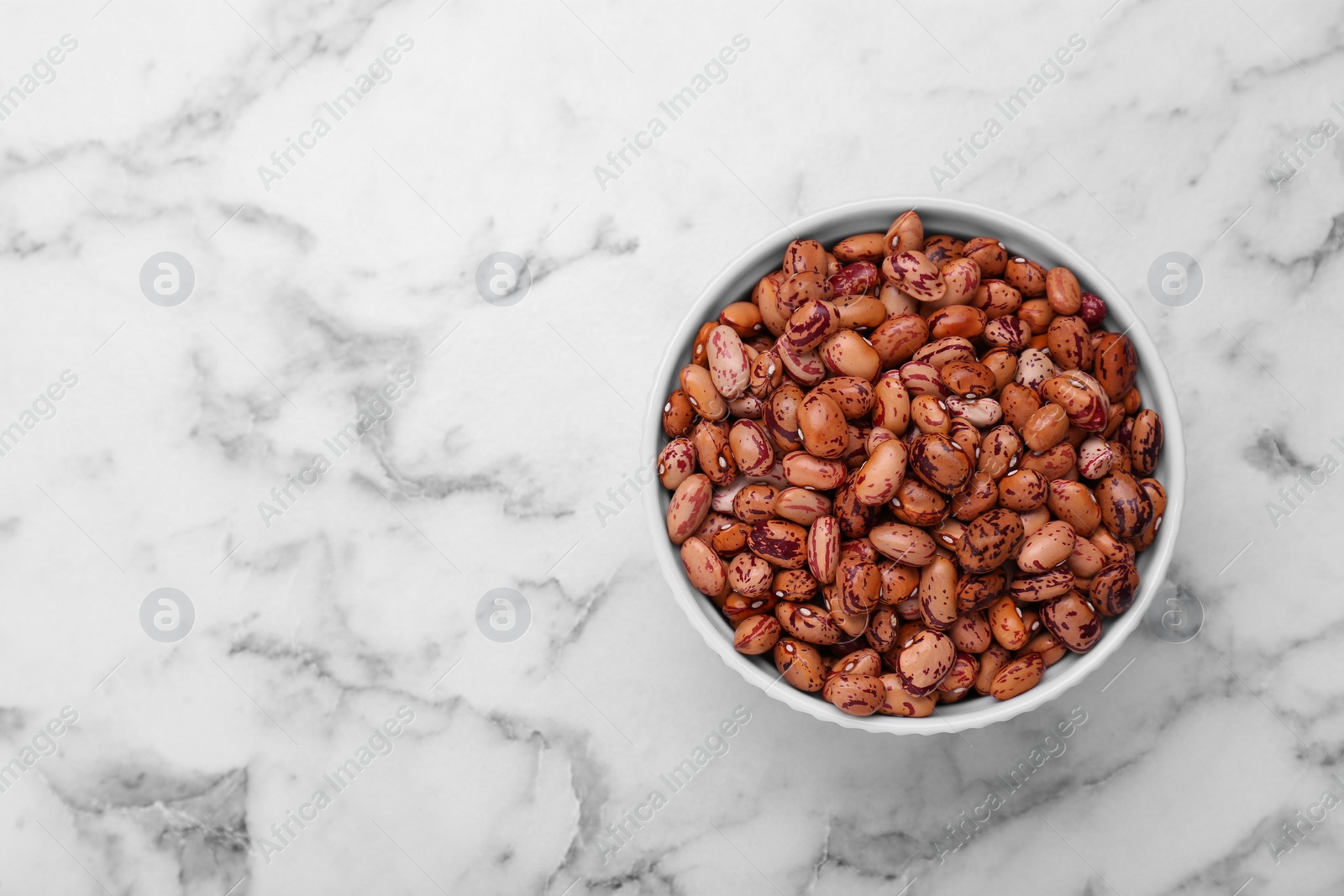 Photo of Bowl with dry kidney beans on white marble table, top view. Space for text