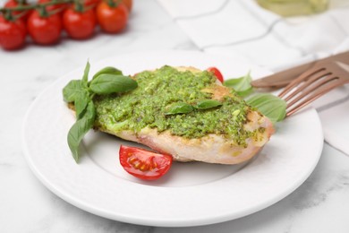 Delicious chicken breast with pesto sauce, tomato and cutlery served on white table, closeup